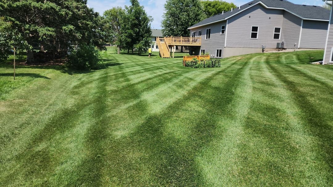 Lush green lawn with striped mowing patterns and a wooden deck in the background.